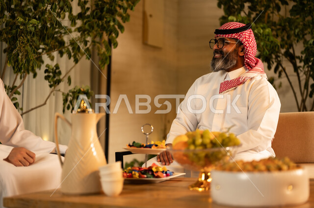 The presentation of Arab hospitality with fruit and coffee, the concept of hospitality and social communication, two Arab Gulf men from Saudi Arabia wearing the thobe and ghutrah are exchanging conversation in a friendly atmosphere, gestures of happiness and joy.