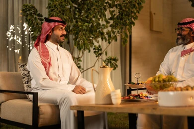 مفهوم الضيافة والتواصل الاجتماعي, رجلان عربيان خليجيان سعوديان يرتديان الثوب والشماغ يقومان بتبادل الحديث في أجواء ودية, تقديم الضيافة العربية مع الفاكهة والقهوة، ايماءات السعادة و السرور،