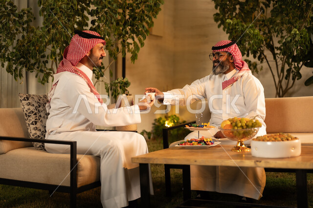 أصالة عادات وتقاليد المجتمع السعودي في المناسبات الاسلامية, كرم الضيافة وحسن الاستقبال في السعودية,رجل عربي خليجي سعودي يرتدي الثوب و الشماغ يقوم يتقديم القهوة الخليجية للضيف, تقديم المشروبات الساخنة العربية الأصيلة في الأعياد