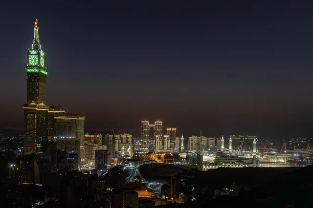 The towers and luxury hotels in Mecca, Saudi Arabia, a close-up of the illuminated Royal Clock Tower at night, the architectural designs of the buildings overlooking the Holy Mosque, landmarks and sacred religious places.