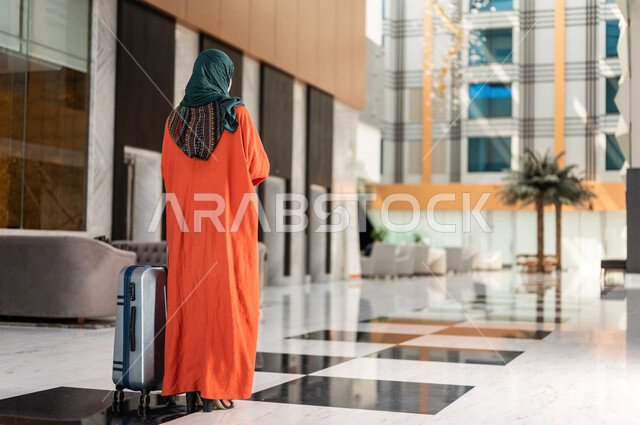 صورة بزاوية من الخلف لسائحة عربية خليجية سعودية تجر حقيبة السفر وتمشي في بهو الفندق ، سيدة أعمال خليجية سعودية ترتدي العباءة الخليجية ، سياحة وفندقة ، قضاء أوقات ممتعة ، رحلة عمل ، سياحة وسفر