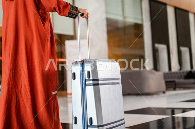 صورة مقربة بزاوية من الخلف لسائحة عربية خليجية سعودية تجر حقيبة السفر وتمشي في بهو الفندق ، سيدة أعمال خليجية سعودية ترتدي العباءة الخليجية ، سياحة وفندقة ، قضاء أوقات ممتعة ، رحلة عمل ، سياحة وسفر