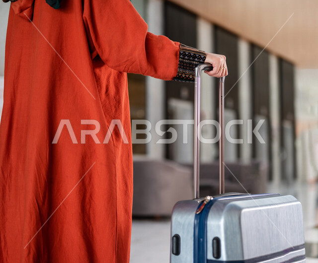صورة مقربة بزاوية من الخلف لسائحة عربية خليجية سعودية تجر حقيبة السفر وتمشي في بهو الفندق ، سيدة أعمال خليجية سعودية ترتدي العباءة الخليجية ، سياحة وفندقة ، قضاء أوقات ممتعة ، رحلة عمل ، سياحة وسفر
