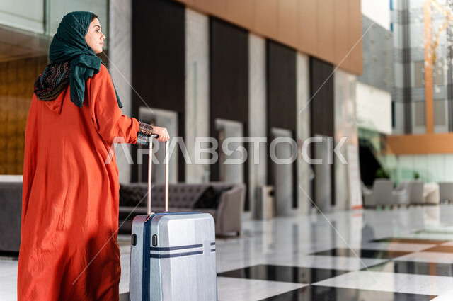 صورة بزاوية من الخلف لسائحة عربية خليجية سعودية تجر حقيبة السفر وتمشي في بهو الفندق ، سيدة أعمال خليجية سعودية ترتدي العباءة الخليجية ، سياحة وفندقة ، قضاء أوقات ممتعة ، رحلة عمل ، سياحة وسفر