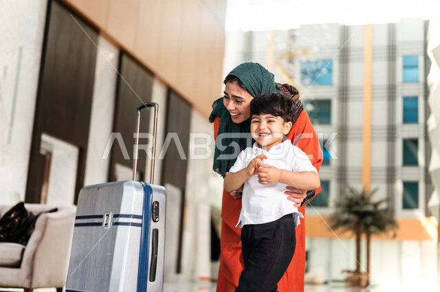A picture of a Saudi Arabian Gulf woman and her son walking in the hotel lobby with travel bag, tourism and hotel, spending the most beautiful times with the family in the best Gulf hotels, entertainment trip, tourism and travel, fun family atmosphere, we
