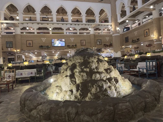 استخدام صخرة كبيرعلى شكل نافورة مياه ، صالة المطعم داخل القرية الشعبية التراثية متحف ومطعم بارز يقع على كورنيش الدمام في المملكة العربية السعودية، مطعم يقدم المأكولات السعودية التقليدية