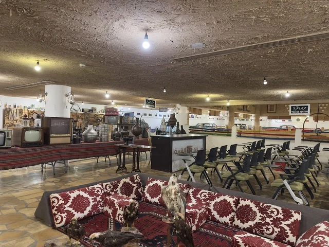 منطقة جلوس تقليدية منخفضة مغطاة بأقمشة منقوشة باللونين الأحمر والأبيض، الحفاظ على التراث المحلي وعرضه للزوار، القرية الشعبية التراثية متحف ومطعم بارز يقع على كورنيش الدمام في المملكة العربية السعودية،  بيئة ريفية أو تاريخية.