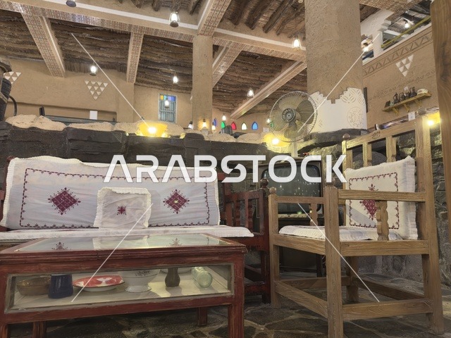 أرائك ومقاعد خشبية بعضها يحتوي على وسائد بيضاء، بيئة ريفية أو تاريخية، الحفاظ على التراث المحلي وعرضه للزوار، القرية الشعبية التراثية متحف ومطعم بارز يقع على كورنيش الدمام في المملكة العربية السعودية