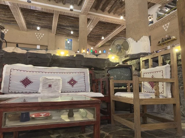 أرائك ومقاعد خشبية بعضها يحتوي على وسائد بيضاء، بيئة ريفية أو تاريخية، الحفاظ على التراث المحلي وعرضه للزوار، القرية الشعبية التراثية متحف ومطعم بارز يقع على كورنيش الدمام في المملكة العربية السعودية