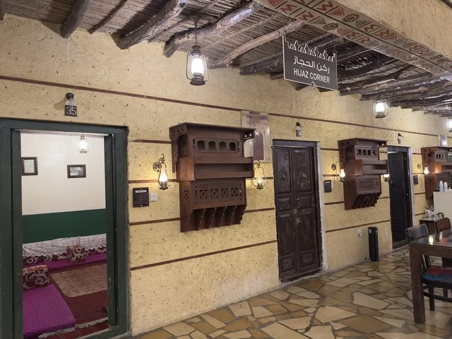 Preserving local heritage and showcasing it to visitors, a sign for the Hijaz corner hanging from a roof made of straw and wood, a rural or historical environment, the traditional folk village is a prominent museum and restaurant located on the Corniche of Dammam in the Kingdom of Saudi Arabia.