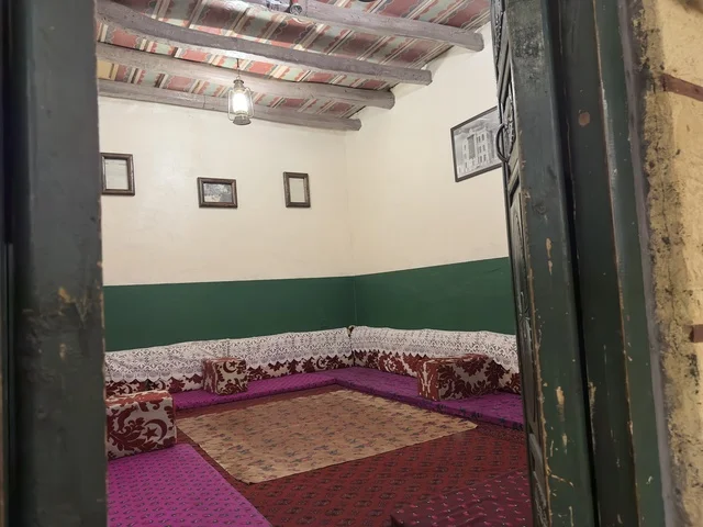 A hotel room inside the heritage village, a sign for the Hijaz corner hanging from a ceiling made of straw and wood, a rural or historical environment, the heritage village is a prominent museum and restaurant located on the Corniche of Dammam in the Kingdom of Saudi Arabia.