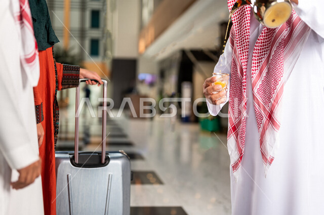 صورة مقربة لرجل سعودي يقوم بتقديم القهوة العربية الساخنة للسيّاح في بهو الفندق السياحي ، سياحة وفندقة ، زوجان سعوديان بإستضافتهم في الفندق ، قضاء أوقات ممتعة ، رحلة زوجية ممتعة ، تقديم حسن الضيافة للزوار الكرام داخل الفندق ، سياحة وسفر