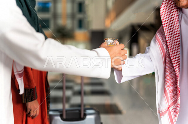 صورة مقربة لرجل سعودي يقوم بتقديم القهوة العربية الساخنة للسيّاح في بهو الفندق السياحي ، سياحة وفندقة ، زوجان سعوديان بإستضافتهم في الفندق ، قضاء أوقات ممتعة ، رحلة زوجية ممتعة ، تقديم حسن الضيافة للزوار الكرام داخل الفندق ، سياحة وسفر