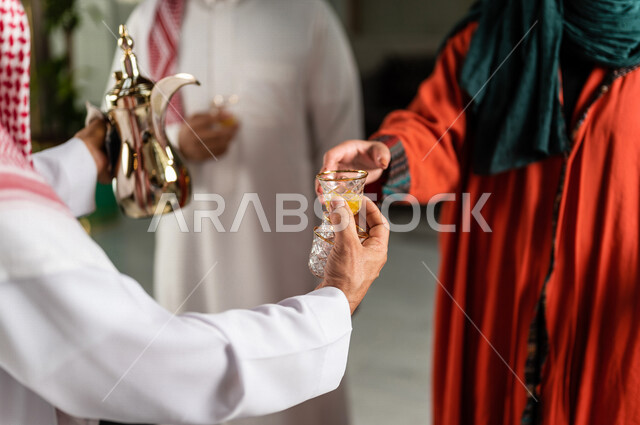 صورة مقربة لرجل سعودي يقوم بتقديم القهوة العربية الساخنة للسيّاح في بهو الفندق السياحي ، سياحة وفندقة ، زوجان سعوديان بإستضافتهم في الفندق ، قضاء أوقات ممتعة ، رحلة زوجية ممتعة ، تقديم حسن الضيافة للزوار الكرام داخل الفندق ، سياحة وسفر