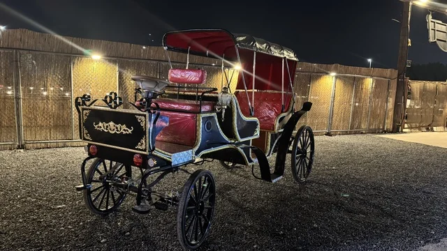 A traditional horse-drawn carriage in the South West (Cowboy) town in the Al-Zahra neighborhood on King Abdulaziz Road in Jeddah in 2025, buildings in the classic Western style, a recreational tourist destination, a place to have a good time in the Kingdom of Saudi Arabia, wearing American cowboy attire.