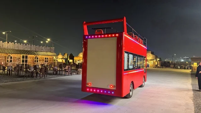 A double-decker tourist bus in the South West (Cowboy) town in the Al-Zahra neighborhood on King Abdulaziz Road in Jeddah for the year 2025, buildings in the classic Western style, a place to have a good time in the Kingdom of Saudi Arabia, wearing American cowboy attire.