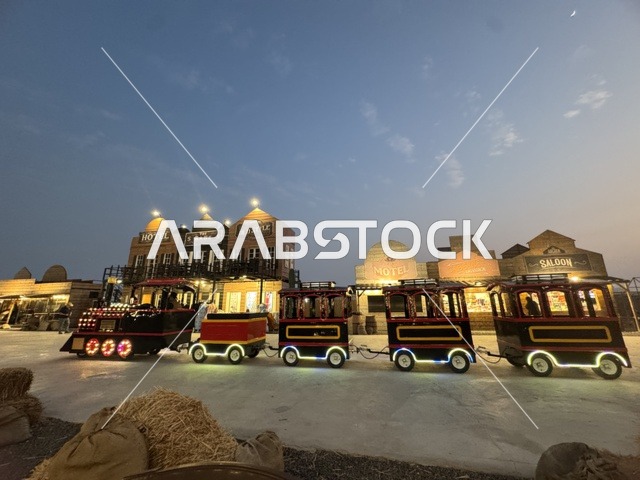 A train for transportation within the South West (Cowboy) town in the Al-Zahra neighborhood on King Abdulaziz Road in Jeddah in 2025, buildings in the classic Western style, a place to have a good time in the Kingdom of Saudi Arabia, wearing American cowboy attire.