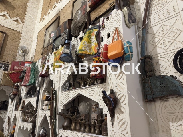 أرفف خشبية بيضاء مزخرفة بنقوش هندسية، الأواني النحاسية أو الفخارية التقليدية الصغيرة على الرفوف، صممت القرية لتعكس العمارة التقليدية للمنطقة، القرية الشعبية التراثية متحف ومطعم بارز يقع على كورنيش الدمام في المملكة العربية السعودية