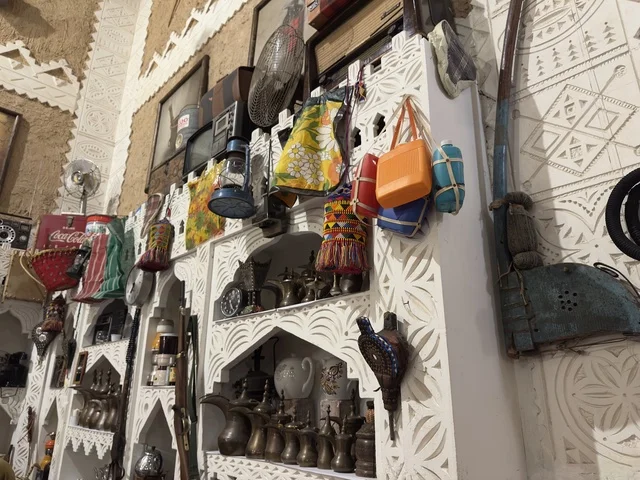 أرفف خشبية بيضاء مزخرفة بنقوش هندسية، الأواني النحاسية أو الفخارية التقليدية الصغيرة على الرفوف، صممت القرية لتعكس العمارة التقليدية للمنطقة، القرية الشعبية التراثية متحف ومطعم بارز يقع على كورنيش الدمام في المملكة العربية السعودية