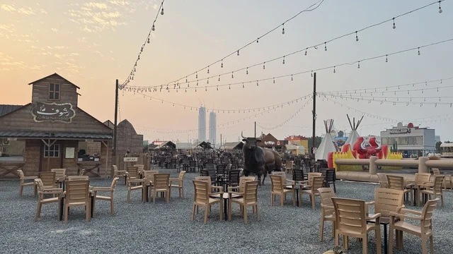 A quiet outdoor session, a recreational tourist destination, the South West (Cowboy) town in the Al-Zahra neighborhood on King Abdulaziz Road in Jeddah in 2025, wearing American cowboy attire, a place to have a good time in the Kingdom of Saudi Arabia, buildings in classic Western style.