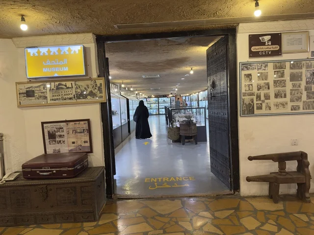 مدخل لمكان متحف أو معرض مع لافتة كُتب عليها "ENTRANCE" (مدخل) على الأرض، صممت القرية لتعكس العمارة التقليدية للمنطقة، القرية الشعبية التراثية متحف ومطعم بارز يقع على كورنيش الدمام في المملكة العربية السعودية