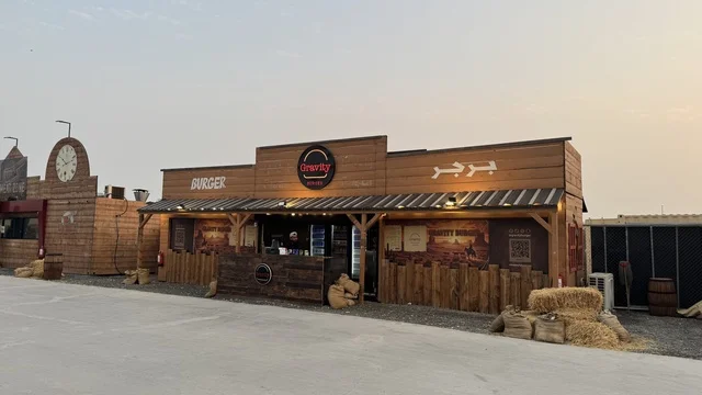 A store selling drinks and snacks in the South West (Cowboy) town in the Al-Zahra neighborhood on King Abdulaziz Road in Jeddah for the year 2025, wearing American cowboy attire, a recreational tourist destination, a place to have a good time in the Kingdom of Saudi Arabia, buildings in the classic Western style.