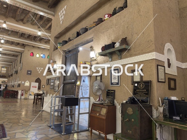 Shelves displaying various items, picture frames, and hanging certificates. The village is designed to reflect the traditional architecture of the region. The heritage folk village is a prominent museum and restaurant located on the Corniche of Dammam in the Kingdom of Saudi Arabia.