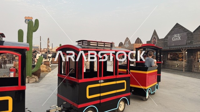 قطار صغير للتنقل في بلدة ساوث ويست (الكاوبوي) في حي الزهراء على طريق الملك عبد العزيز في مدينة جدة لعام 2025، ارتداء زي الكاوبوي الامريكية، وجهه سياحية ترفيهية، مكان لقضاء وقت ممتع في المملكة العربية السعودية، مباني على الطراز الكلاسيكي الغربي