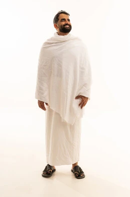 الوقوف بإستقامة والنظر الى شيء ما، الاستعداد لأداء مناسك العمرة في شهر رمضان المبارك، بورتريه لرجل عربي خليجي سعودي مبتسم يرتدي لباس الاحرام يقوم بزيارة بيت الله الحرام في مكة المكرمة، العبادة والتقرب الى الله، صورة الجسم بالطول الكامل، خلفية بيضاء