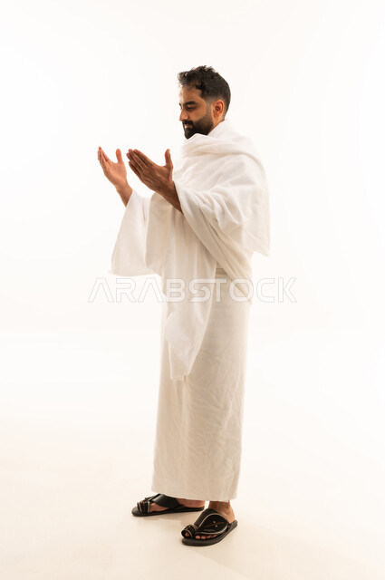 التضرع إلى الله تعالى، تعابير التوسل والاسترحام، طلب المساعدة من المولى عز وجل، مفهوم الاجتهاد في العبادة، ، بورتريه  لرجل عربي خليجي سعودي يرتدي ملابس الاحرام يرفع ييه بايماءات الدعاء، آداء مناسك الحج والعمرة، صورة لكامل الجسم، خلفية بيضاء