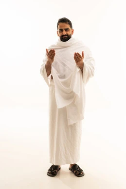 The concept of the pillars of Islam, supplication and humility to the Lord of the servants, performing the rituals of Hajj and Umrah, worship and drawing closer to God, a portrait of a Saudi Arabian Gulf man wearing the Ihram garment raising his hands in gestures of supplication, full-body, white background.