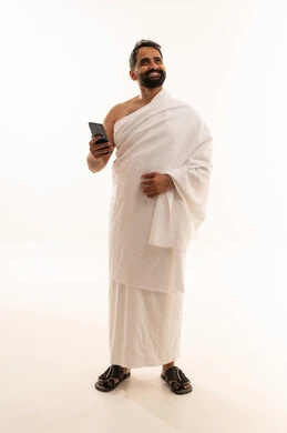 الدعاء عبر الهاتف المحمول, بورتريه لرجل مسلم سعودي خليجي عربي يرتدي ملابس الاحرام يمسك بيدية الجوال، الدليل الالكتروني للحاج و المعتمر, استخدام تطبيقات الجوال للتواصل مع العائلة والأصدقاء, الجسم بالطول الكامل، خلفية بيضاء