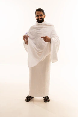 الركن الخامس من أركان الاسلام لمن استطاع اليه سبيلا، الوقوف وشرب ماء زمزم بعد اداء الفريضه والنافله في مكه المكرمه، الاستعداد لاداء مناسك الحج والعمره والتقرب الى الله بالاعمال الصالحه، بورتريه لرجل عربي خليجي سعودي يرتدي ثوب الاحرام، الجسم بالطول الكامل، خلفية بيضاء