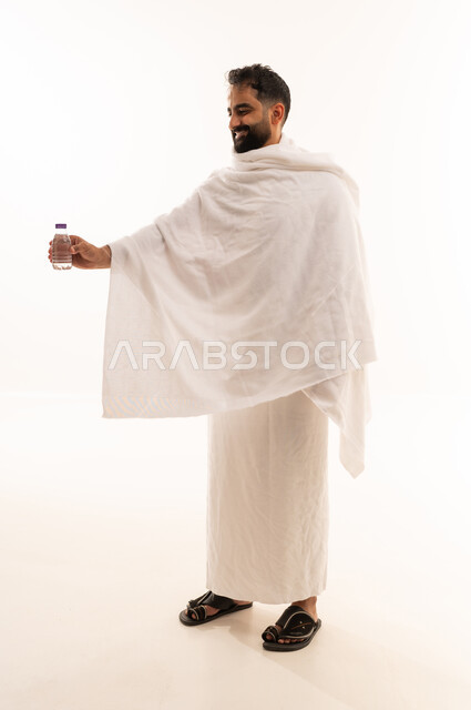 الاستعداد لاداء مناسك الحج والعمره والتقرب الى الله بالاعمال الصالحه، بورتريه لرجل عربي خليجي سعودي يرتدي ثوب الاحرام، الوقوف وشرب ماء زمزم بعد اداء الفريضه والنافله في مكه المكرمه، الركن الخامس من أركان الاسلام لمن استطاع اليه سبيلا، الجسم بالطول الكامل، خلفية بيضاء