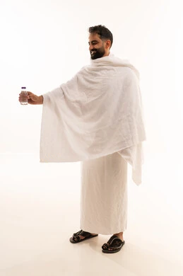 Preparation for performing the rituals of Hajj and Umrah and getting closer to God through good deeds, a portrait of an Arab Gulf Saudi man wearing the Ihram garment, standing and drinking Zamzam water after performing the obligatory and voluntary prayers in the holy city of Mecca, the fifth pillar of Islam for those who are able to do so, full-body, white background.