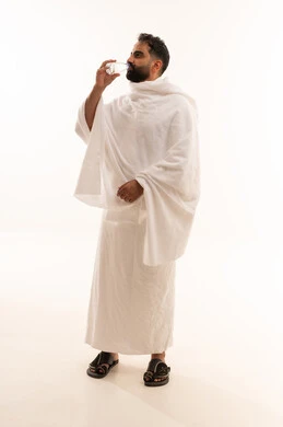 Performing the rituals of Hajj and Umrah, increasing fluid intake to keep the body hydrated, a portrait of an Arab Saudi Gulf man wearing the Ihram attire drinking fresh water, quenching his thirst with Zamzam water, full-body shot, white background.