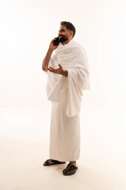 Communication with family and friends using a mobile phone, a portrait of a young Gulf Arab Saudi man wearing Ihram clothing making a call through his mobile device, full-body image, white background.