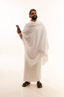الدليل الالكتروني للحاج و المعتمر، النظر الى شيء ما، الدعاء عبر الهاتف المحمول, بورتريه لرجل مسلم سعودي خليجي عربي يرتدي ملابس الاحرام ويجري مكالمة فيديو, استخدام تطبيقات الجوال للتواصل مع العائلة والأصدقاء, الجسم بالطول الكامل، خلفية بيضاء