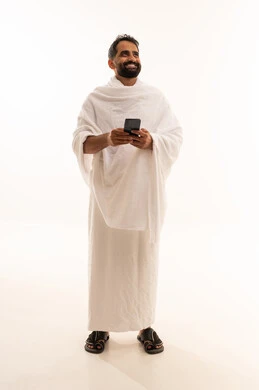 النظر الى شيء ما، الدعاء عبر الهاتف المحمول, بورتريه لرجل مسلم سعودي خليجي عربي يرتدي ملابس الاحرام ويجري مكالمة فيديو, الدليل الالكتروني للحاج و المعتمر, استخدام تطبيقات الجوال للتواصل مع العائلة والأصدقاء, الجسم بالطول الكامل، خلفية بيضاء