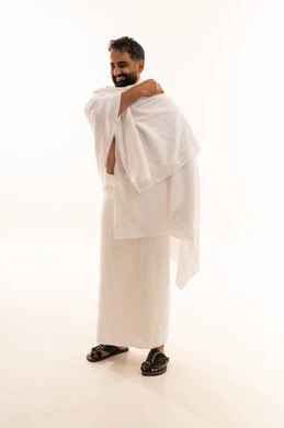ايماءات السعادة و السرور، مفهوم العبادة والتقرب إلى الله، الطهارة والسكينة الروحية، بورترية لرجل عربي خليجي سعودي مسلم يرتدي لباس الإحرام الأبيض يقوم بتعديل ثيابة استعداد لأداء مناسك الحج أو العمرة، الجسم بالطول الكامل، خلفية بيضاء