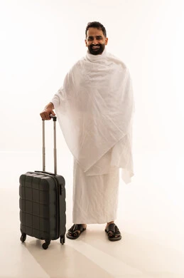 اداء فريضة الحج والعمرة، النظر الى الكاميرا بتعابير السرور، الاستعداد للتوجه و الانطلاق لزيارة بيت الله الحرام، بورتريه لرجل خليجي عربي سعودي مبتسم يرتدي ملابس الاحرام ويمسك بيده حقيبة السفر، الجسم بالطول الكامل، خلفية بيضاء