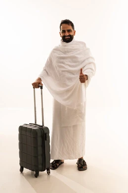 Expressions of agreement and acceptance, looking at the camera with gestures of excitement to reach Mecca, preparing to head out and embark on a visit to the Sacred House of God, a portrait of a smiling Gulf Arab Saudi man wearing Ihram clothing and holding a travel bag, performing the pilgrimage and Umrah, full-body shot, white background.