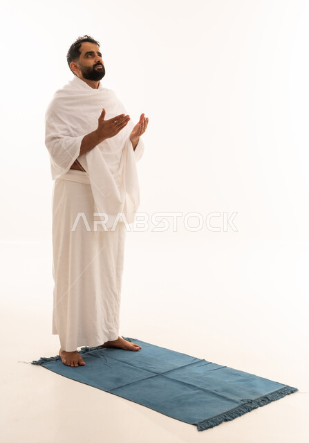 طلب العفو والمغفرة من الله تعالى، رفع الكفين نحو الأعلى والدعاء، العبادة والطاعة والإكثار من الأذكار, أداء مناسك الحج والعمرة، بورتريه لرجل عربي خليجي يرتدي ملابس الإحرام يدعو الله، الجسم بالطول الكامل، خلفية بيضاء