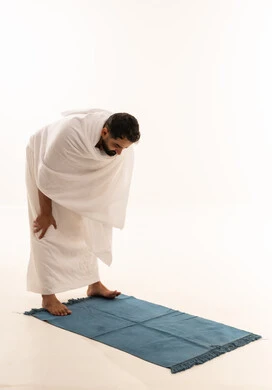 الخشوع في الصلاة والتضرع إلى الله، اداء الركن الثاني من اركان الاسلام الخمسه, بورتريه لرجل عربي خليجي يرتدي ملابس الإحرام يؤدي فريضة الصلاة على سجادته الخاصه, مناسك الحج والعمرة، التقرب إلى الله بالطاعه والعبادات، خلفية بيضاء