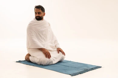 العبادة والتقرب إلى الله، إقامة الصلوات على وقتها، أداء الفرائض الدينية الاسلامية، مفهوم أركان الإسلام، بورتريه لرجل عربي سعودي خليجي يرتدي لباس الاحرام يجلس على سجادة الصلاة, خلفية بيضاء