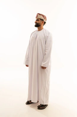 تعابير الثقة بالنفس، النظر الى شيء ما بايماءات السرور، مفهوم الرجولة والوقار، الاهتمام بالمظهر الخارجي، بورتريه لرجل عربي خليجي عماني يرتدي الدشداشة والعمامة يقف باستقامة، صورة الجسم بالطول الكامل، خلفية بيضاء