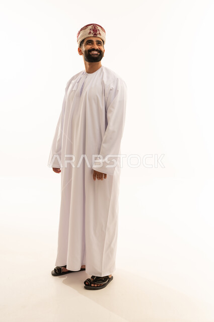 Looking at something with gestures of joy, expressions of self-confidence, the concept of masculinity and dignity, attention to appearance, a portrait of an Arab Gulf Omani man wearing a dishdasha and a turban standing upright, full-body image, white background.