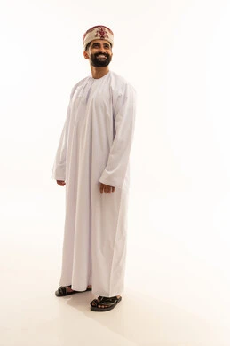 النظر الى شيء ما بايماءات السرور، تعابير الثقة بالنفس، مفهوم الرجولة والوقار، الاهتمام بالمظهر الخارجي، بورتريه لرجل عربي خليجي عماني يرتدي الدشداشة والعمامة يقف باستقامة، صورة الجسم بالطول الكامل، خلفية بيضاء