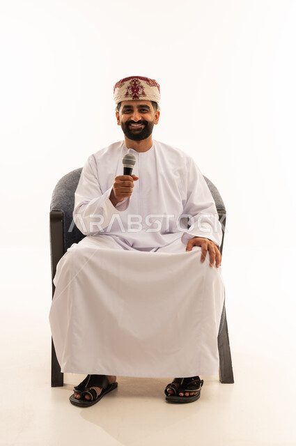 التدريب الصوتي وتقديم البرامج الاذاعيه، فن إلقاء الخطابات والندوات، بورتريه لرجل عربي خليجي عماني يرتدي الدشداشة و العمامة يجلس على الكرسى يمسك بيدية الميكروفون، ايماءات وتعابير وجه و يدين تعبر عن الغناء والطرب، خلفية بيضاء