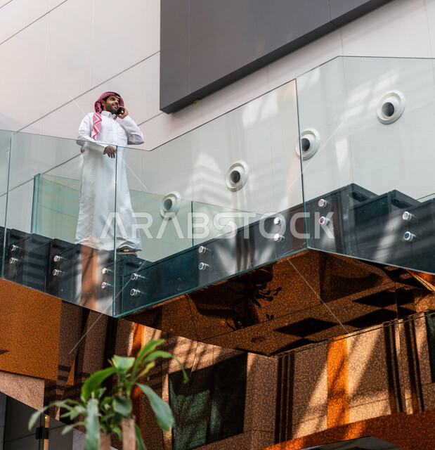 A Saudi Gulf man, making a phone call via a mobile phone inside the tourist hotel, using modern technical equipment, a working session, the concept of business management, making business deals, working remotely, e-marketing, a business trip, tourism and